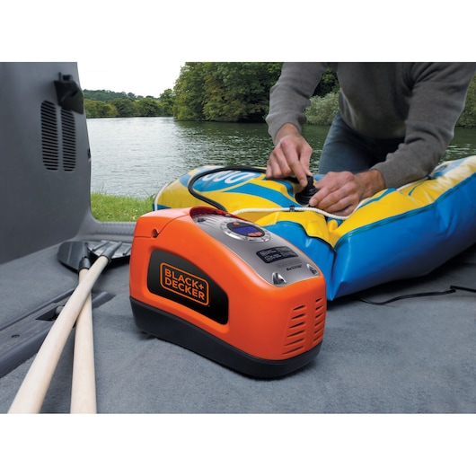 BLACKDECKER ASI300 portable orange air compressor inflating a blue and yellow raft near a lake.