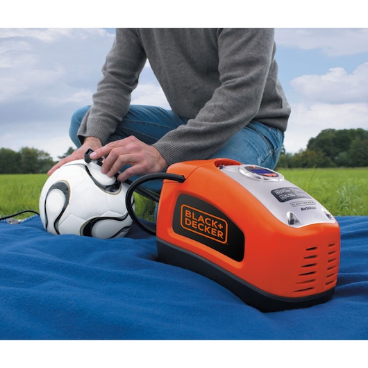 BLACK+DECKER ASI300 air compressor inflating a soccer ball outdoors, orange and black color, on blue blanket.