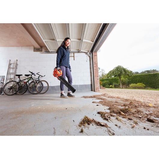 BLACKDECKER BCBL200L leaf blower in use, cleaning debris from garage floor, outdoor setting.