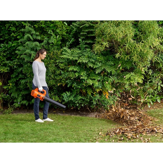 BLACKDECKER BCBL200L leaf blower in use outdoors, orange and black design, blowing leaves on grass.