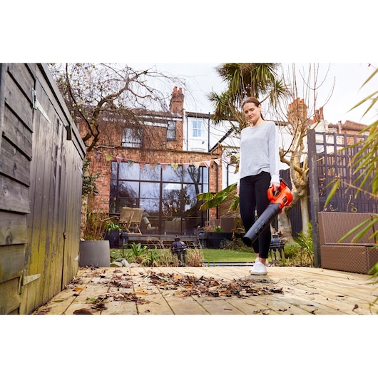 BLACKDECKER BCBL200L leaf blower held by person clearing leaves on wooden deck in garden.