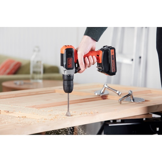 BLACK+DECKER BCD001C1 cordless drill in use drilling into wood, hand gripping handle, indoor setting.
