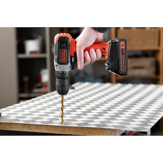 BLACK+DECKER BCD001C1 cordless drill with 18V lithium battery drilling into metal sheet, side view.