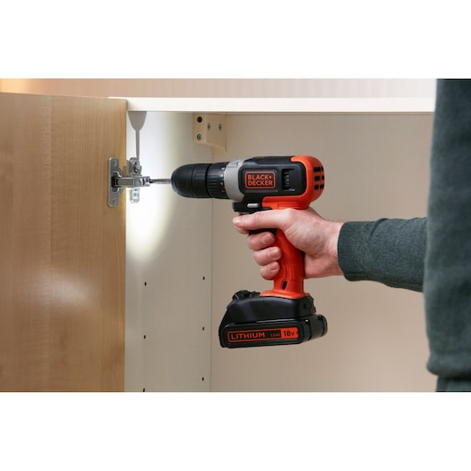 BLACK+DECKER BCD001C1 cordless drill driver being used to assemble wooden cabinet, side view.