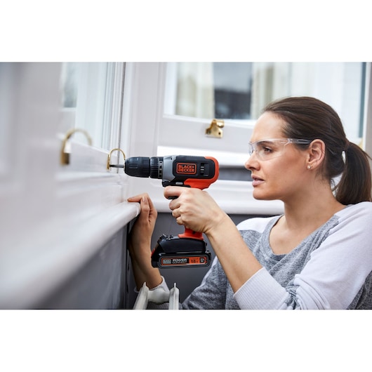 Photo of BLACK+DECKER BCD001C1 cordless drill being used to drill into a window frame indoors.