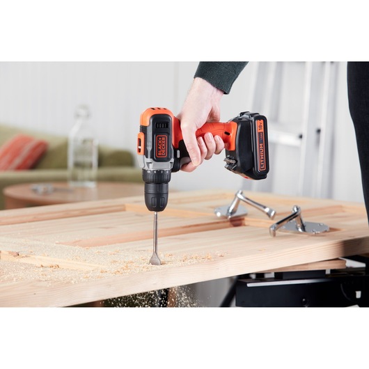 BLACK+DECKER BCD002C1 cordless drill being used to drill into a wooden board indoors, close-up view.
