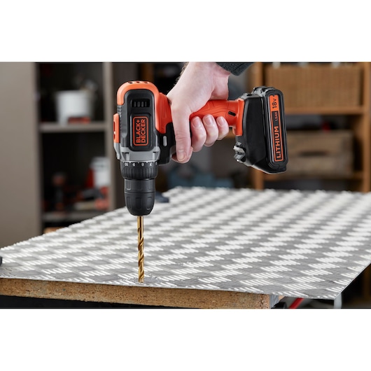 BLACK+DECKER BCD002C1 cordless drill being used to drill into a metal sheet, close-up view.