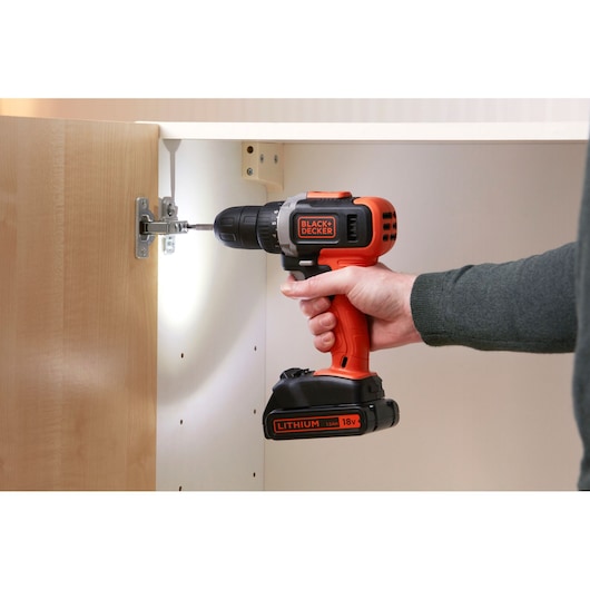 BLACKDECKER BCD002C1 cordless drill in use assembling a cabinet, close-up with visible 18V lithium battery.