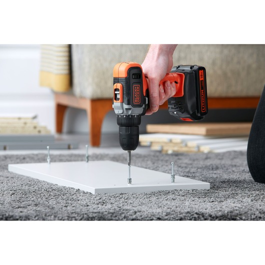 Photo of BLACK+DECKER BCD002C2K cordless drill being used to assemble white furniture panel on carpet.