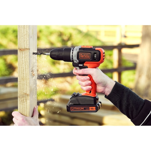 BLACKDECKER BCD003C1 cordless drill in use, drilling into wood outdoors, orange and black design.