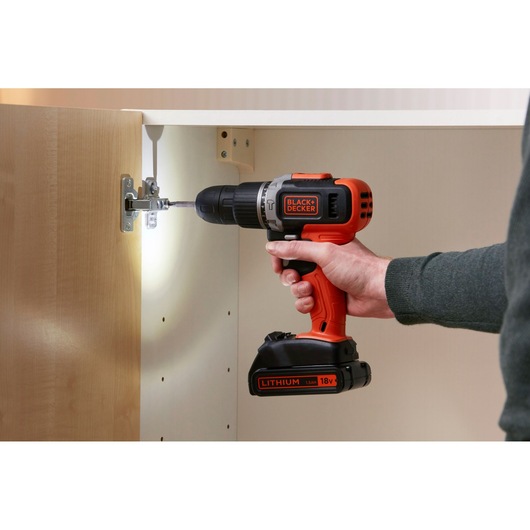 BLACK+DECKER BCD003C1 cordless drill used to install cabinet hinge, orange and black design, side angle.