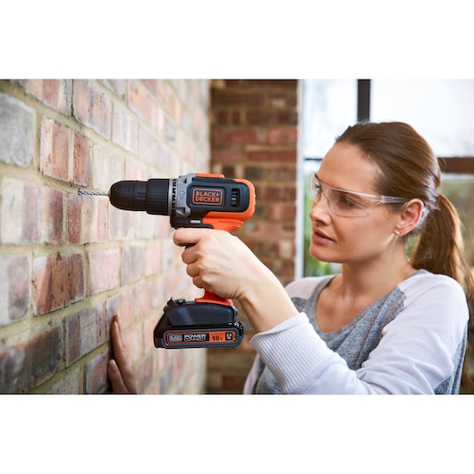 Photo of BLACK+DECKER cordless drill BCD003C1 in use drilling into a brick wall, close-up view.