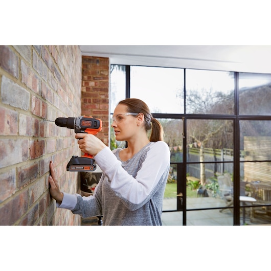 BLACKDECKER BCD003C1 cordless drill used on brick wall indoors, product in hand, clear battery pack visible