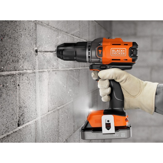 Gloved hand using a BLACK+DECKER cordless drill to drill a hole in a concrete wall.