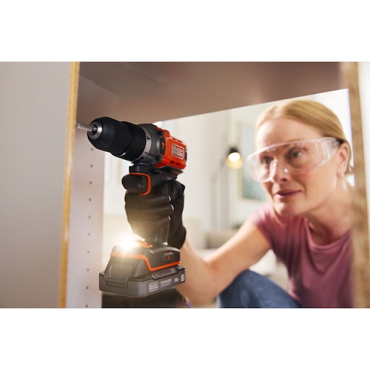 BLACK+DECKER BCD383D1 cordless drill used for assembling furniture, person wearing gloves.