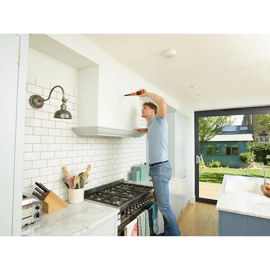 BLACKDECKER BCF603C cordless screwdriver used in a modern kitchen next to stove with white tile backsplash.