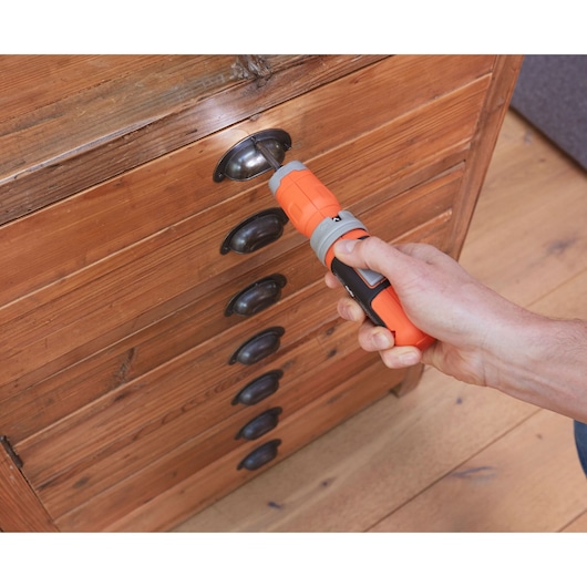 BLACKDECKER BCF603C orange cordless screwdriver in use on wooden drawer handle.