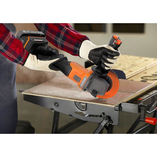 BLACKDECKER BCG6L8D2S cordless angle grinder in use cutting tile, worker wearing gloves and plaid shirt.