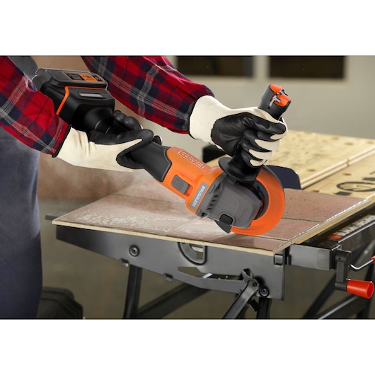 BLACKDECKER BCG6L8F1S cordless angle grinder cutting tile on workbench, operator wearing gloves.