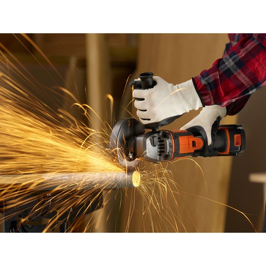 Photo of BLACKDECKER BCG720M1 cordless angle grinder cutting metal pipe, sparks flying, close-up action shot.