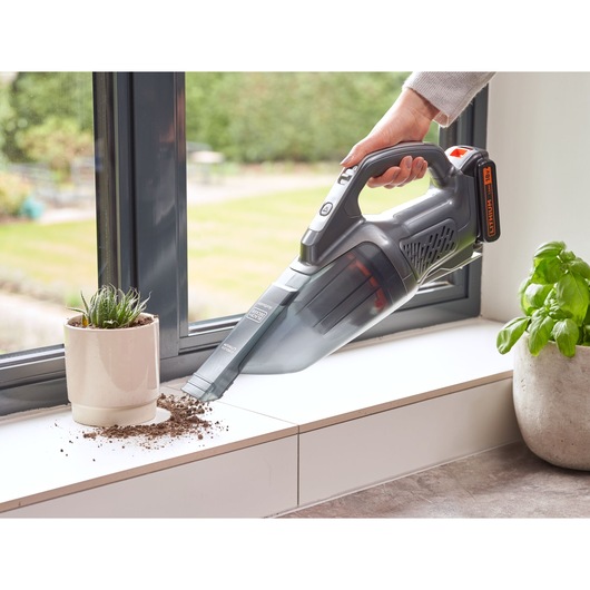 BLACKDECKER BCHV001C1 cordless handheld vacuum cleaning soil on a white windowsill, front angle.
