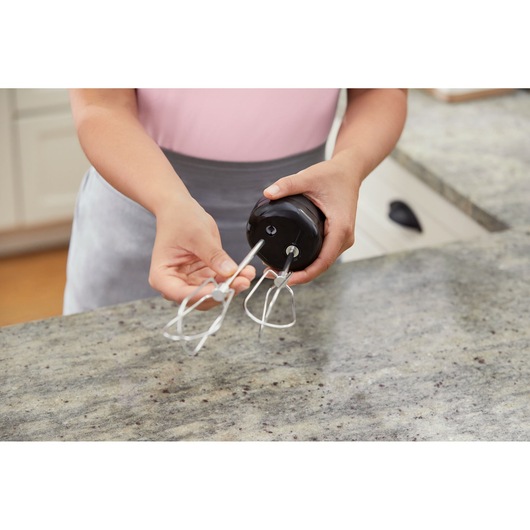 BLACK+DECKER BCKM101HM hand mixer being assembled on kitchen counter, close-up of hands and metal beaters.
