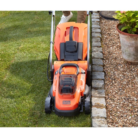 BLACKDECKER BCMW33184L2 cordless lawn mower in orange, top view on grass near stone border.