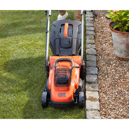 Photo of BLACKDECKER BCMW3336L1 lawn mower cutting grass near stone border in garden.