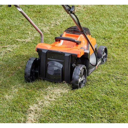 BLACKDECKER BCMW3336L1 lawn mower rear view on grass, orange and black body, wide rear wheels.
