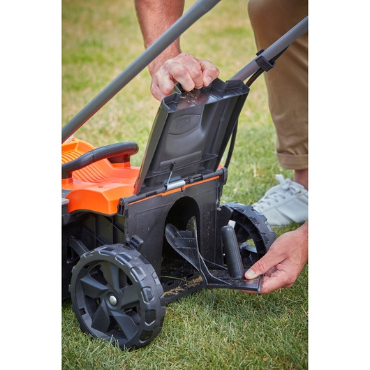 BLACKDECKER BCMW3336L2 lawn mower close-up, hands opening rear chute cover, shown on grass.