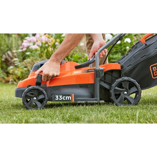 Photo of BLACKDECKER BCMW3336N cordless lawn mower, 33cm cutting width, close-up of handle adjustment in garden.