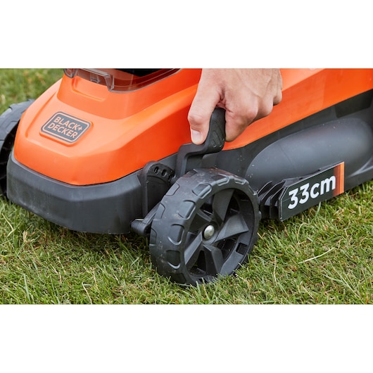 BLACK+DECKER BCMW3336N lawn mower side view, hand adjusting wheel height, orange and black, 33cm cutting width.