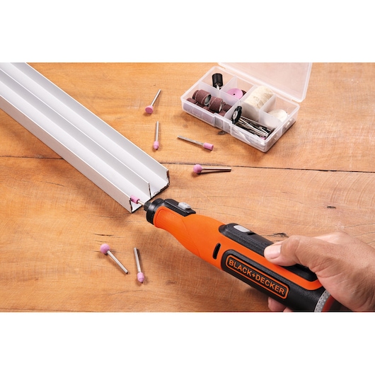 BLACK+DECKER BCRT8IK rotary tool kit with orange handle in use on metal, assorted accessories and case on table.