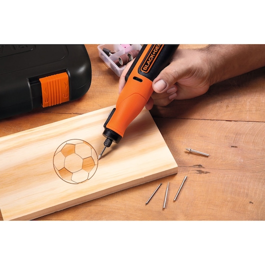 BLACK+DECKER BCRT8IK rotary tool engraving a soccer ball design on wood, accessories and case visible.
