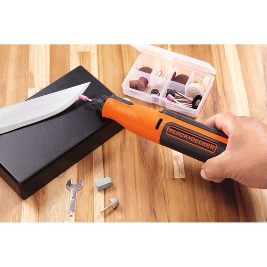 Photo of BLACK+DECKER BCRT8I rotary tool in use with accessory kit, sharpening a knife on wooden surface.