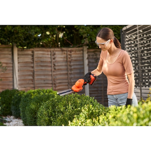 BLACKDECKER BCSS18B hedge trimmer in use outdoors trimming green bushes.