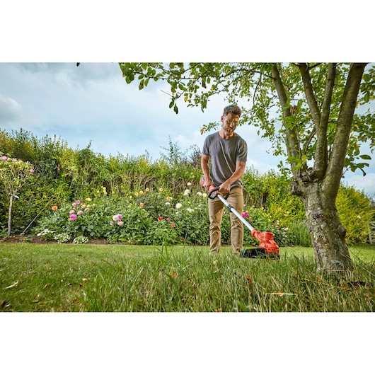 BLACKDECKER grass trimmer BCSTA536L1 in use on lawn near tree and flowerbed, outdoor garden setting.