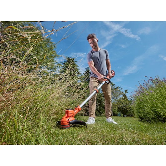BLACKDECKER BCSTA536L1 grass trimmer in use cutting tall grass outdoors, battery-powered design visible.