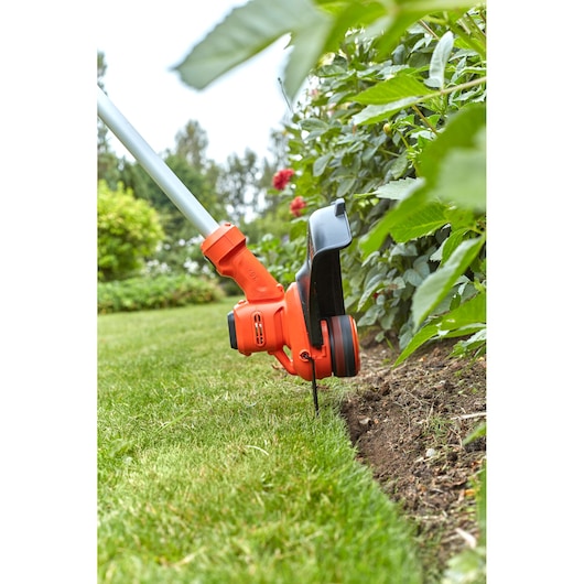 BLACKDECKER BCSTA536L1 grass trimmer close-up in use edging lawn beside flower bed outdoors.