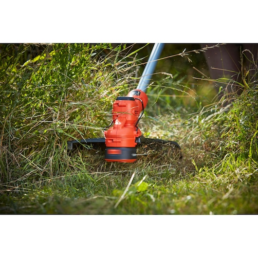 BLACKDECKER BCSTA536L1 orange cordless grass trimmer cutting tall grass outdoors.