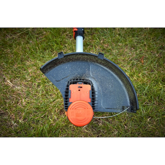 BLACKDECKER BCSTA536L1 grass trimmer head with orange line feed system, shown close-up on grass.