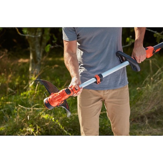 Photo of a person holding a BLACK+DECKER BCSTA536L1 cordless grass trimmer outdoors, focusing on the handle and shaft.