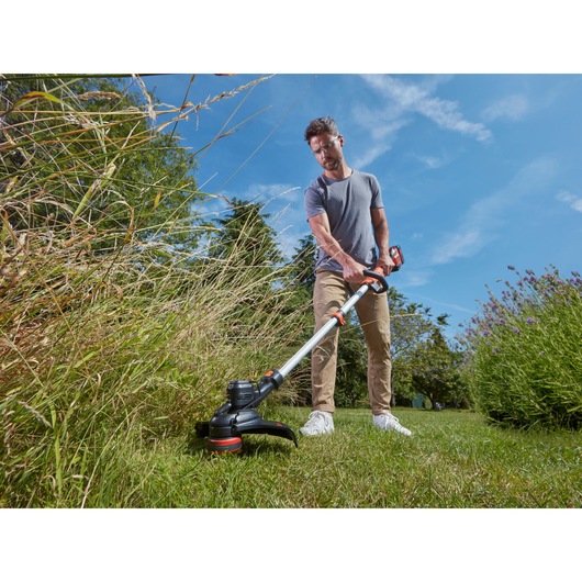 BLACKDECKER BCSTE636L1 cordless grass trimmer in use outdoors cutting tall grass, photography.