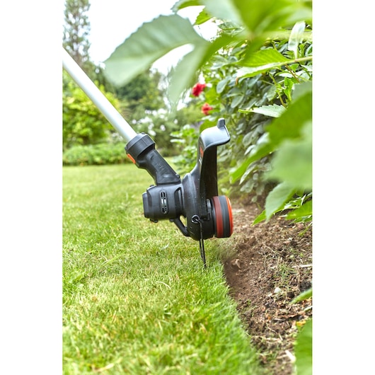 BLACKDECKER BCSTE636L1 grass trimmer used to edge lawn near garden plants outdoors.
