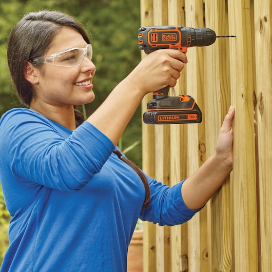 Photo of BLACKDECKER BDCDC18K cordless drill in use drilling wood outdoors, orange and black design.