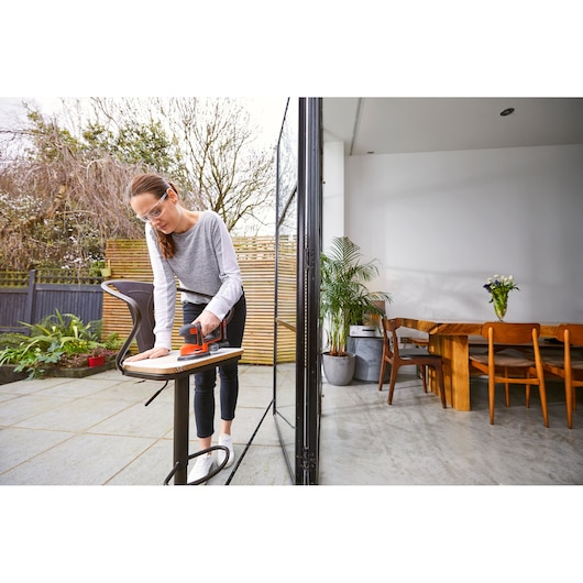 Photo of BLACKDECKER BDCDS18N sander in use on a wooden surface outdoors near a modern patio table.