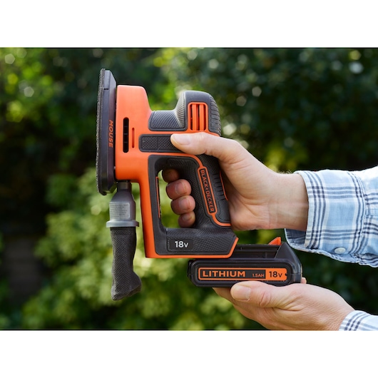 BLACKDECKER BDCDS18 cordless mouse sander, orange and black, held outdoors, 18V lithium battery visible.