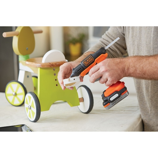 Photo of BLACKDECKER BDCGG12N cordless glue gun in use assembling a green wooden toy with white accents.