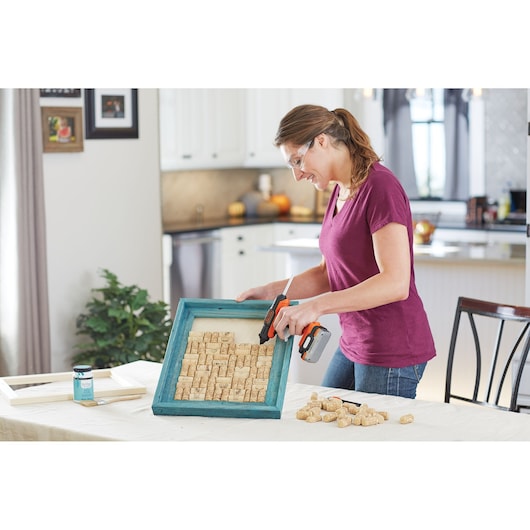 BLACKDECKER BDCGG12N cordless glue gun used for crafting with corks in a blue wooden frame on table.