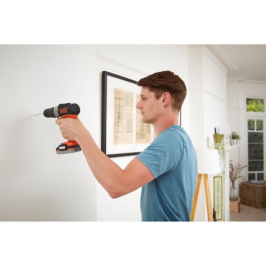 Photo of BLACKDECKER BDCHD12S1 cordless drill in use on a white wall indoors.